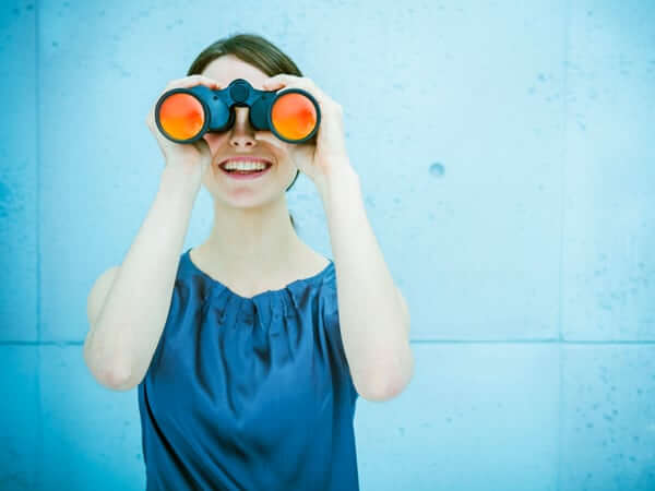 Junge Frau mit Fernglas schaut in die Kamera